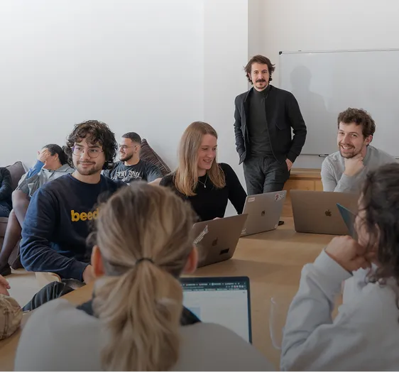 Groupe de jeunes professionnels travaillant ensemble autour d'une table avec des ordinateurs portables dans une salle de réunion lumineuse.